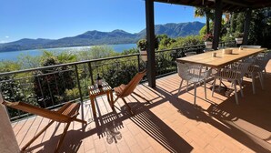 Una terraza con mesa y sillas de madera, una silla colgante y vistas a montañas y un lago.