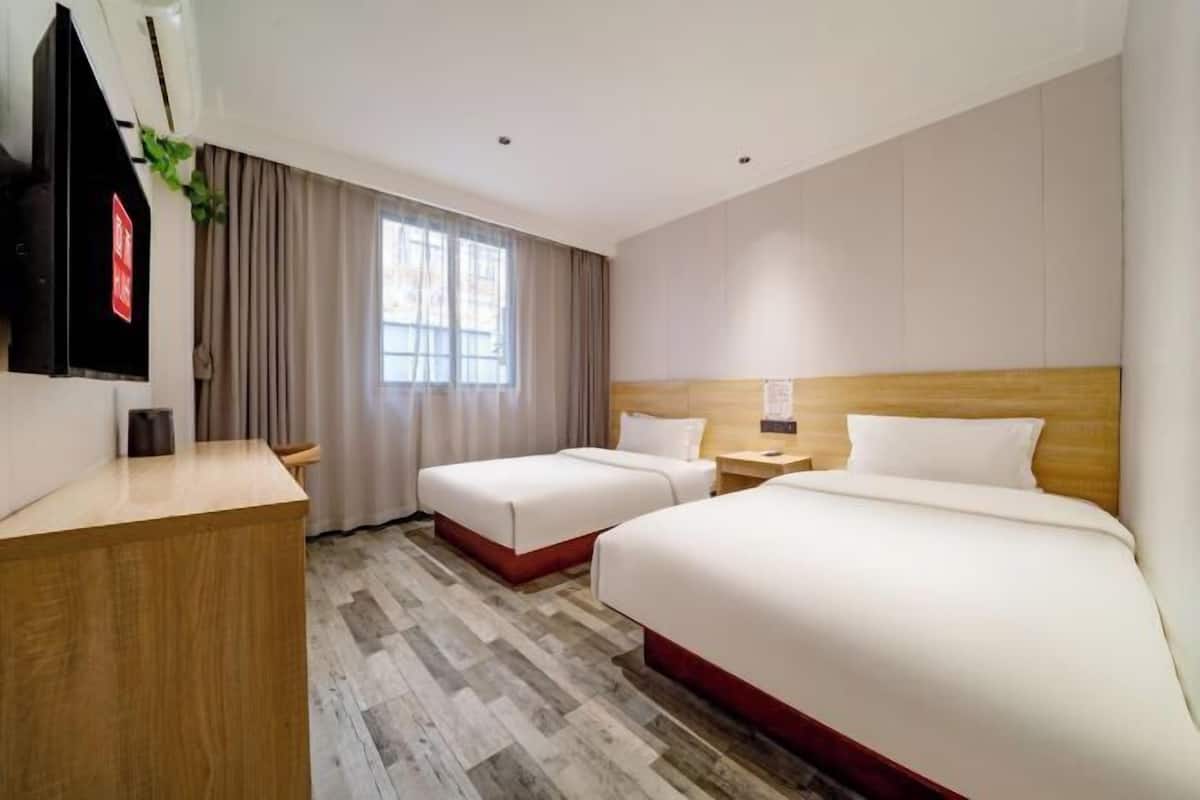 Una habitación de hotel con dos camas, un escritorio de madera, un televisor y una ventana con cortinas.