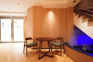 Un hall d’hôtel avec une table ronde en bois et des chaises, un comptoir d’accueil et un escalier dont le mur est illuminé de lumière bleue.