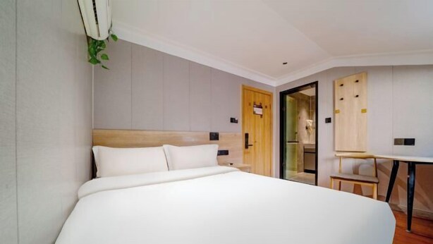 Une chambre d’hôtel moderne avec un grand lit, une tête de lit en bois, une petite table et un miroir.