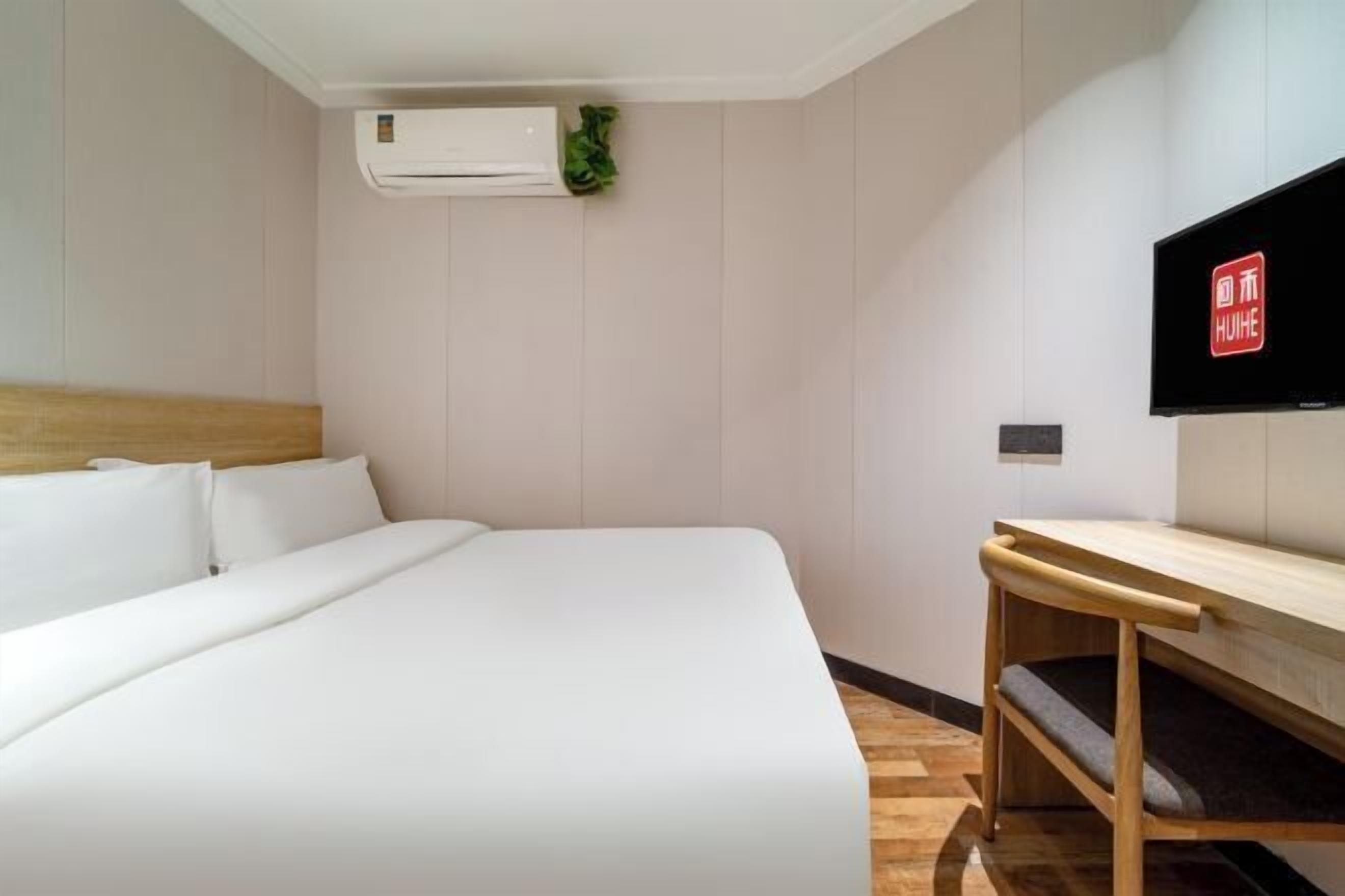 Een hotelkamer met een bed, een houten bureau, een flatscreen televisie en een airconditioning.