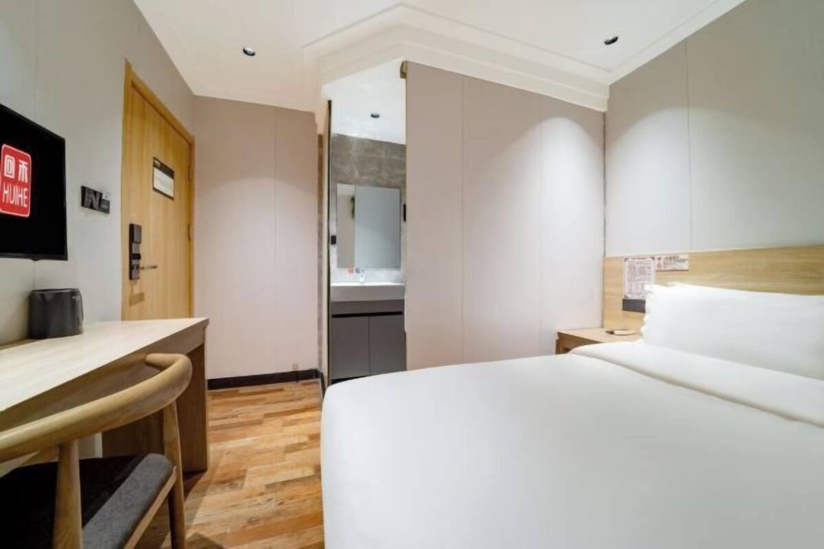 Habitación de hotel con cama, escritorio, silla, televisor, puerta de madera y baño visible a través de una puerta abierta.