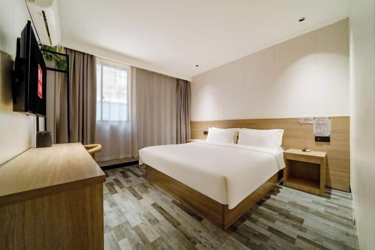 Una habitación de hotel con cama, escritorio, televisor y ventana con cortinas.