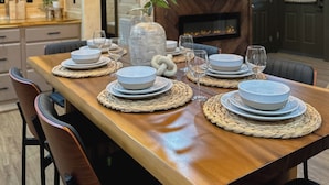 A wooden dining table set with plates, glasses, and a vase with a plant.