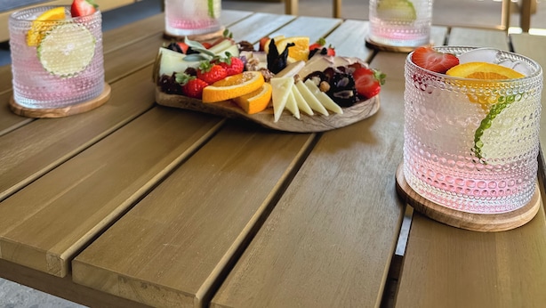 A wooden table with a fruit platter and three glasses of pink beverage.