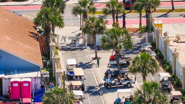 A beachfront hotel with a blue building, palm trees, and a beach in the background.