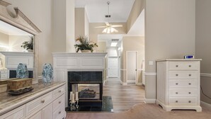 A well-lit hallway with a fireplace, a mirror, a dresser, and a clock on the wall.