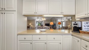 A modern kitchen with white cabinetry, a coffee maker, and a dining area with chairs and a table.
