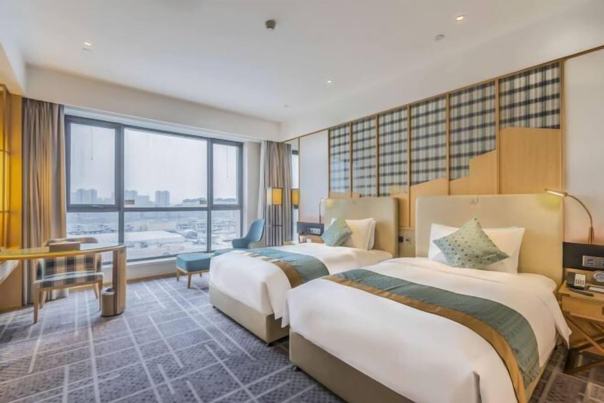 Une chambre d’hôtel avec deux lits, un bureau et une grande fenêtre donnant sur la ville.
