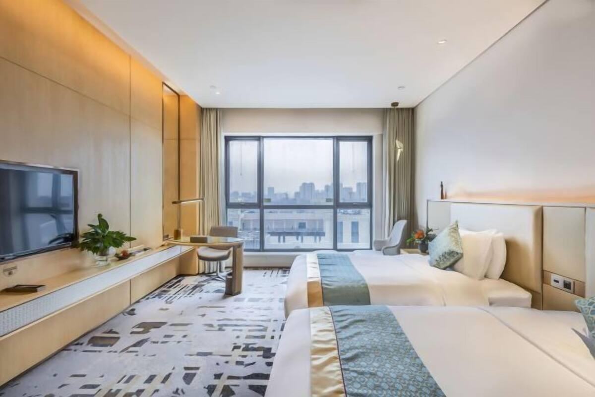 Une chambre d  ’hôtel avec une grande fenêtre, un lit, un bureau avec une télévision et une chaise.