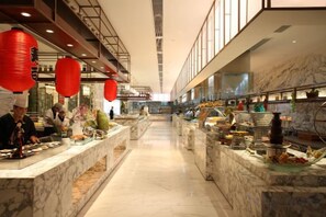 Un hall d’hôtel avec des comptoirs en marbre, des lanternes rouges et un long couloir.