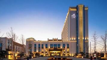 Un hotel moderno con una imponente torre vertical, una entrada central y un área ajardinada al frente.