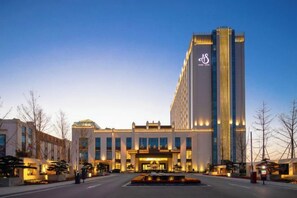 Un hôtel moderne doté d’une tour verticale imposante, d’une entrée centrale et d’un espace paysager aménagé à l’avant.