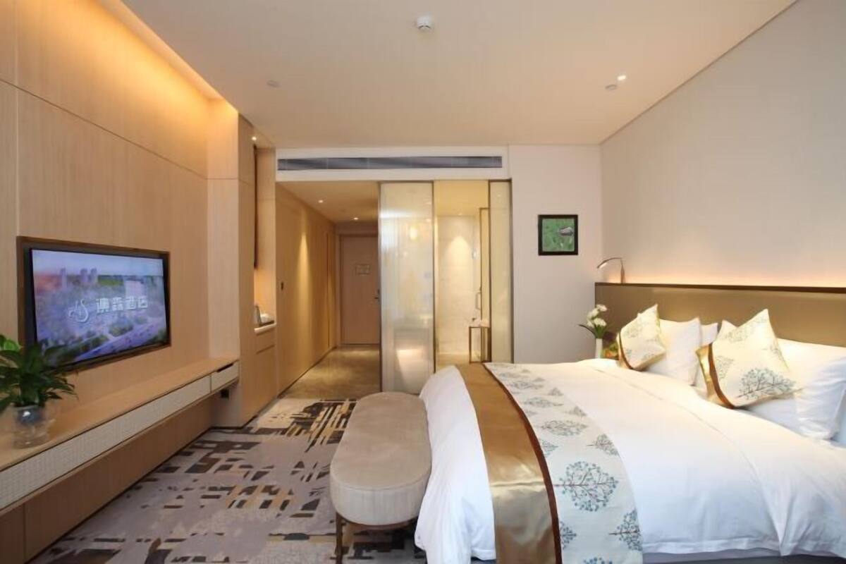 Une chambre d’hôtel avec un lit, une télévision, un banc et une porte donnant sur une autre pièce.