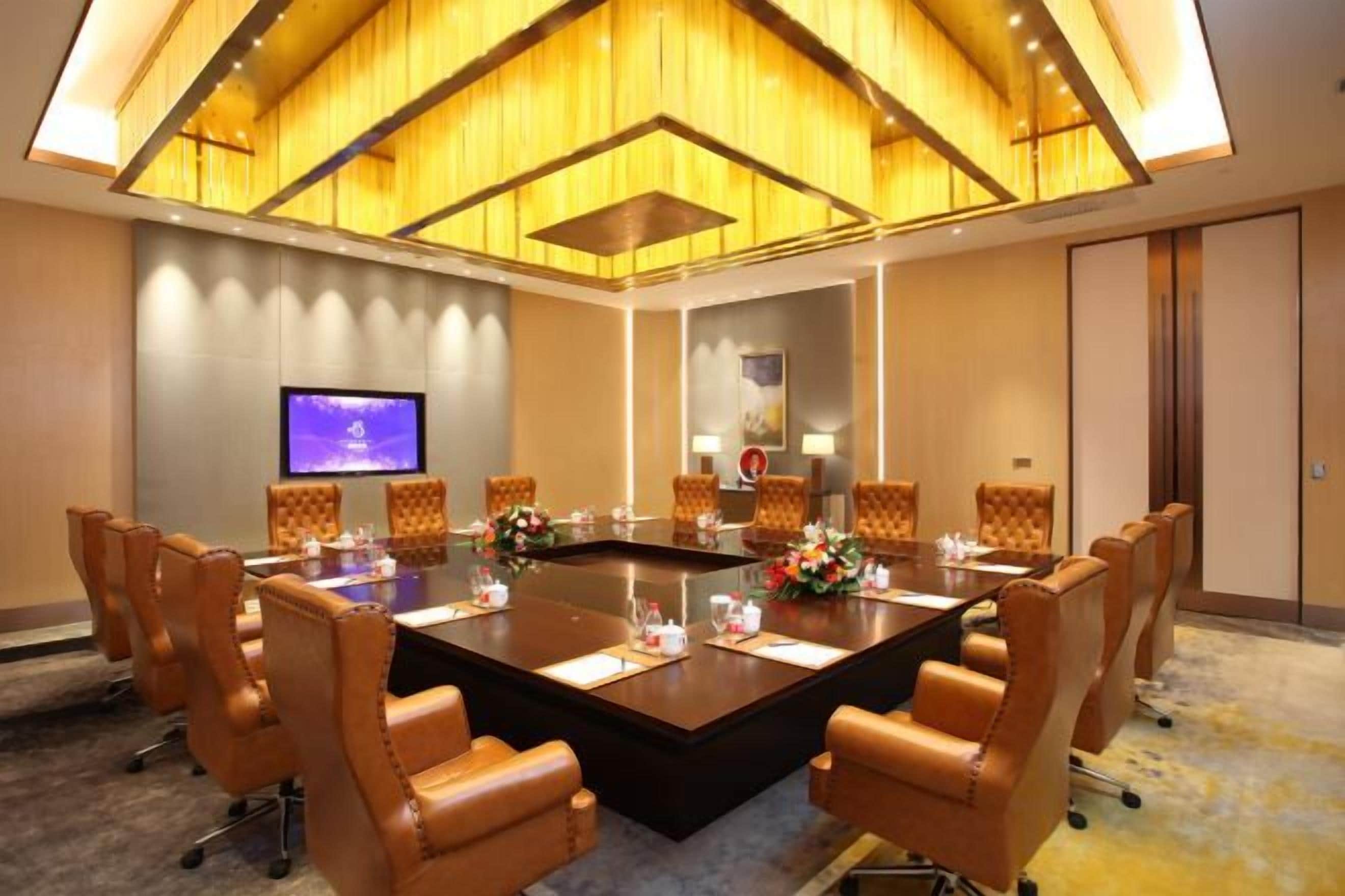 Une salle de conférence dotée d’une grande table, de fauteuils en cuir, d’un téléviseur à écran plat et d’un plafond orné de panneaux de bois.