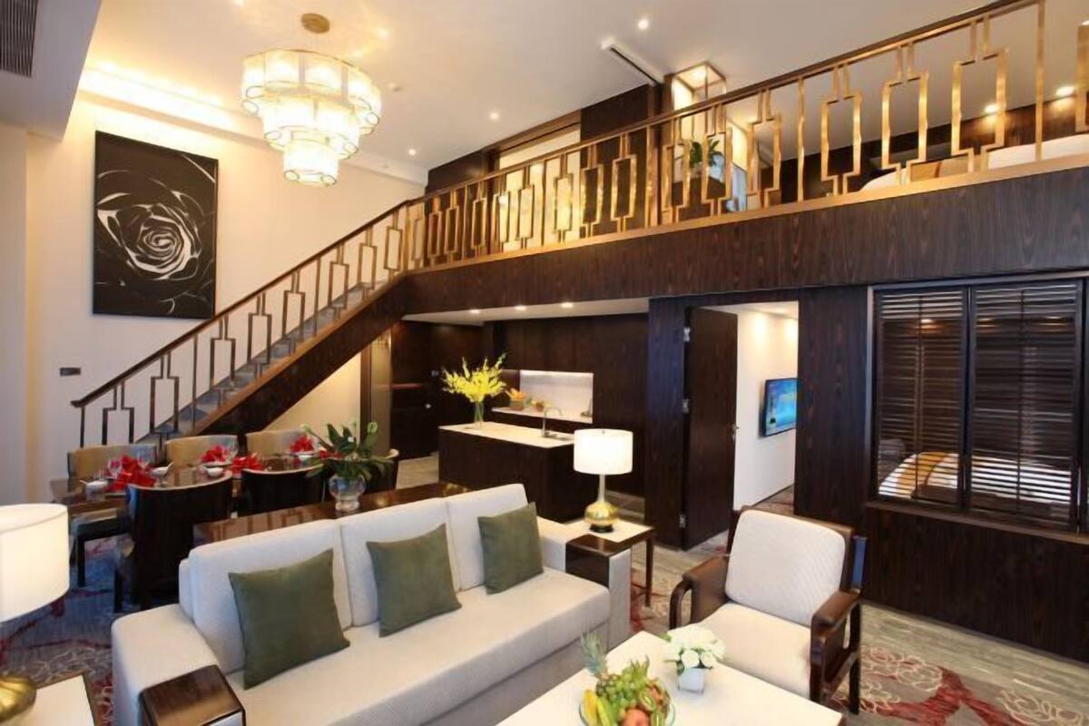 Un grand espace de vie comprenant un escalier, un canapé, une table à manger décorée de fleurs et un coin cuisine.