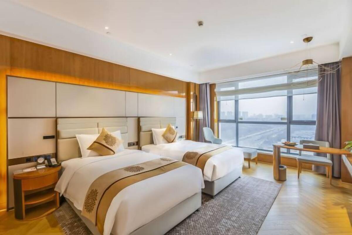 Une chambre d’hôtel moderne avec deux lits, un bureau et une grande fenêtre donnant sur la ville.