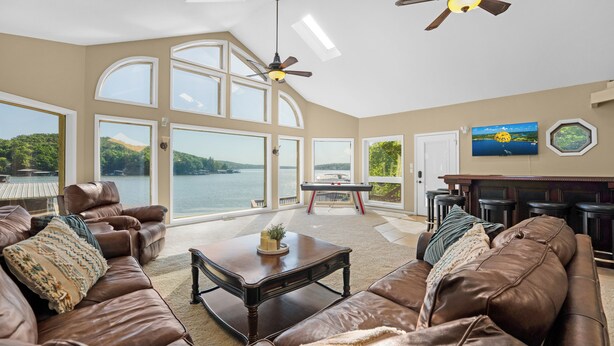 A spacious living room with a large window overlooking a lake, leather sofas, a coffee table, and a fireplace. - Lakeside Paradise! Private Dock w/ Hot Tub! (Jasper Township)