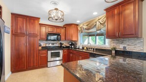 A kitchen with wooden cabinets, stainless steel appliances, a granite countertop, and a window with curtains. - Lakeside Paradise! Private Dock w/ Hot Tub! (Jasper Township)