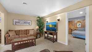 A living room with a sofa, coffee table, TV, and a sign reading "The Rhodes Family Lake House Established 2025". - Lakeside Paradise! Private Dock w/ Hot Tub! (Jasper Township)