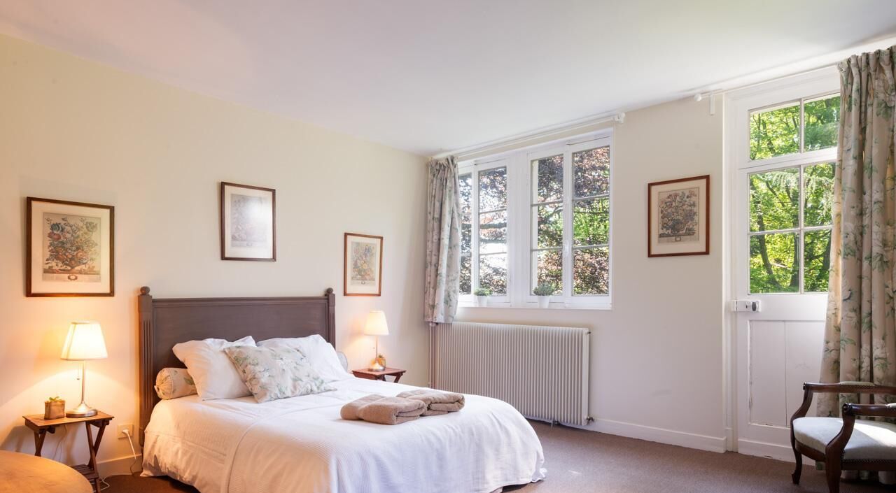 Een slaapkamer met een groot bed, twee bedlampen, een radiator en lijstwerken aan de muren.