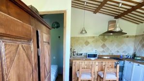 Une cuisine avec un sol en pierre, des meubles de rangement en bois, un coin bar avec des tabourets et un luminaire suspendu.