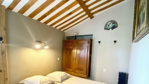 Une chambre avec un plafond en bois, un lit recouvert de linge de lit blanc, une armoire en bois et un petit objet décoratif accroché au mur.