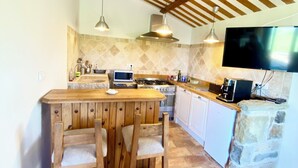 Une cuisine avec un îlot central en bois, des tabourets de bar, un téléviseur et des éléments décoratifs en pierre.