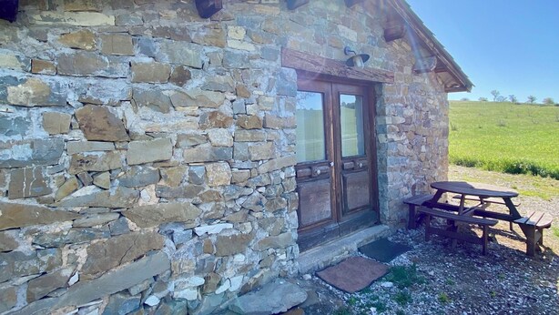 Un bâtiment en pierre avec une porte en bois et une table de pique-nique à l’extérieur.