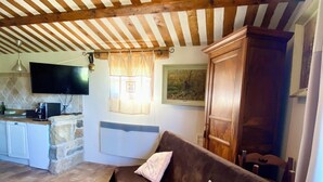Un salon chaleureux avec un canapé marron foncé, deux coussins, un mur en pierre, un téléviseur à écran plat, un meuble en bois et un sol carrelé.
