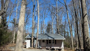 A small, single-story cabin with a gabled roof, surrounded by tall trees and a gravel driveway. - Heister Valley House (Richfield)