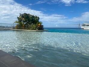 A clear pool with a tropical island and a view of the ocean and city skyline.