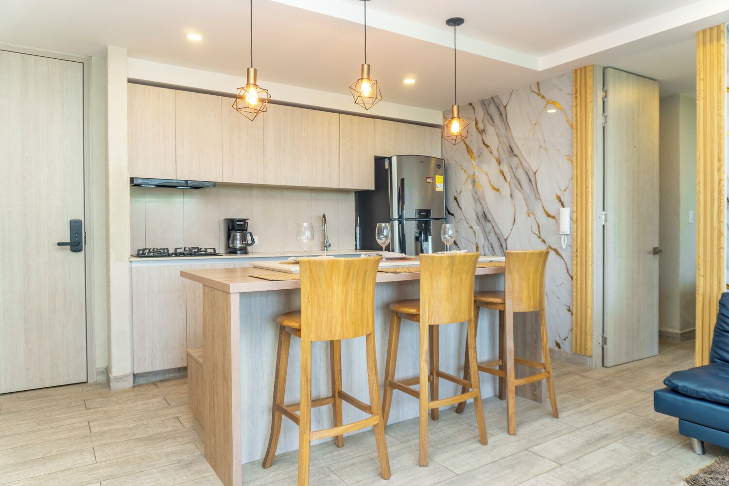 Una cocina moderna con armarios de madera, una isla central con taburetes de bar, una estufa empotrada y un refrigerador.