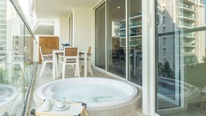 Een balkon met een jacuzzi, eettafel, stoelen en uitzicht op een modern gebouw.
