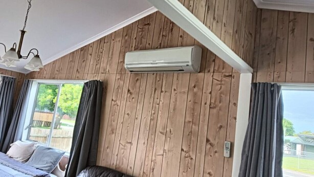 Ein Zimmer mit einem Bett, einem Deckenventilator, einer Klimaanlage und einem Fenster mit Vorhängen.