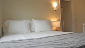 Ein ordentlich bezogenes Bett mit weißen Leinen und einer grauen Streifenwolldecke.