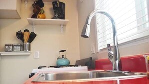 Eine Küche mit roter Arbeitsplatte, einem Edelstahl-Spülbecken, einem blauen Wasserkocher und einem Küchenutensilien-Hängeregal.