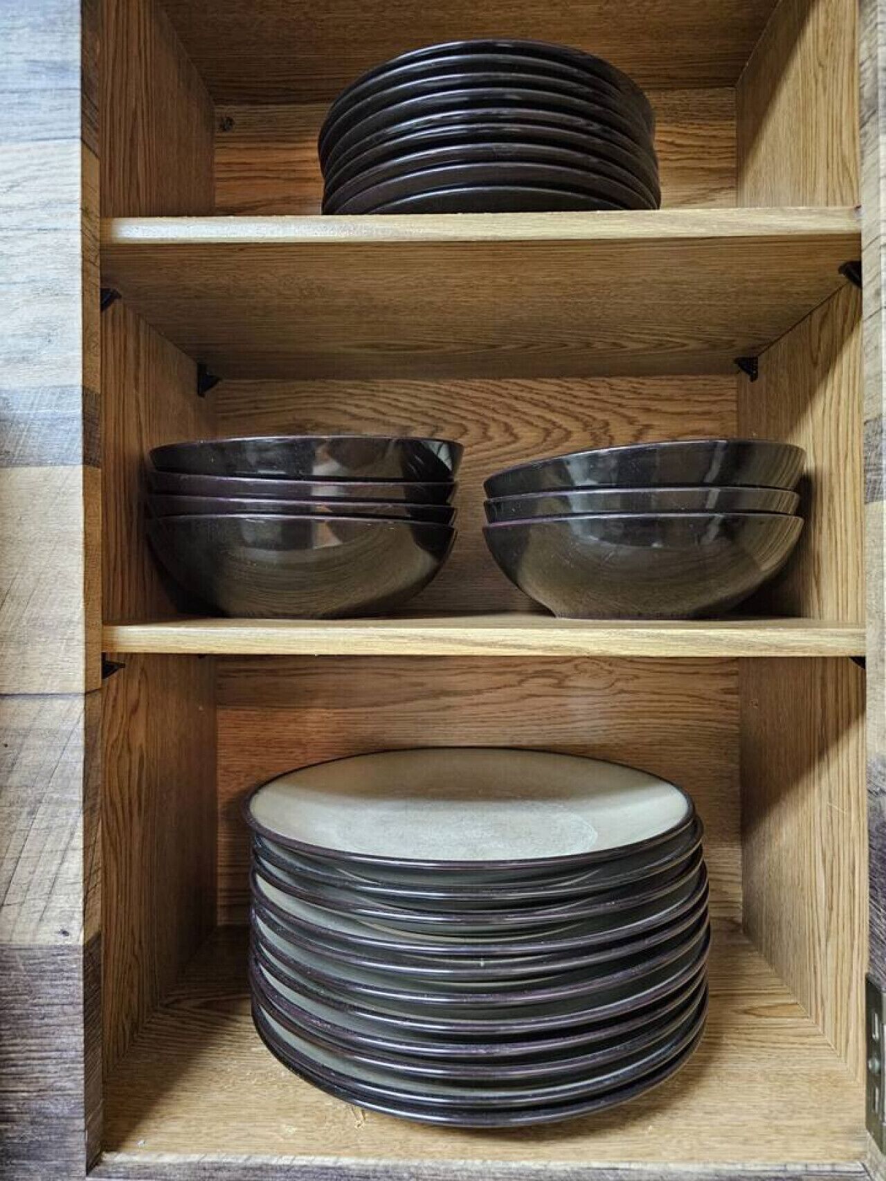 Una estantería de madera con tres repisas, cada una con cuencos y platos apilados.