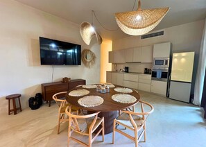Uma cozinha moderna com área de refeições, uma televisão de tela plana e um grande candeeiro de fibra natural.