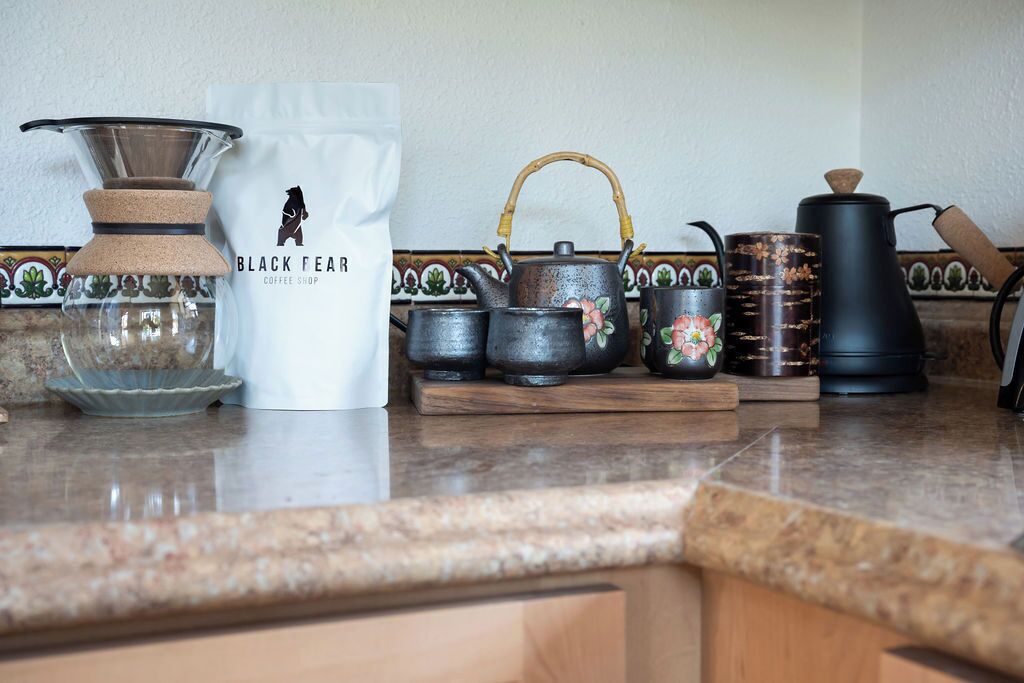Un comptoir de cuisine avec une machine à café, une théière, une bouilloire et un sac de café étiqueté « Black Feather Coffee Shop ».