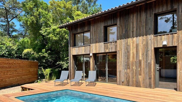 Ein modernes Holzhaus mit Pool und Sitzgelegenheit im Freien.