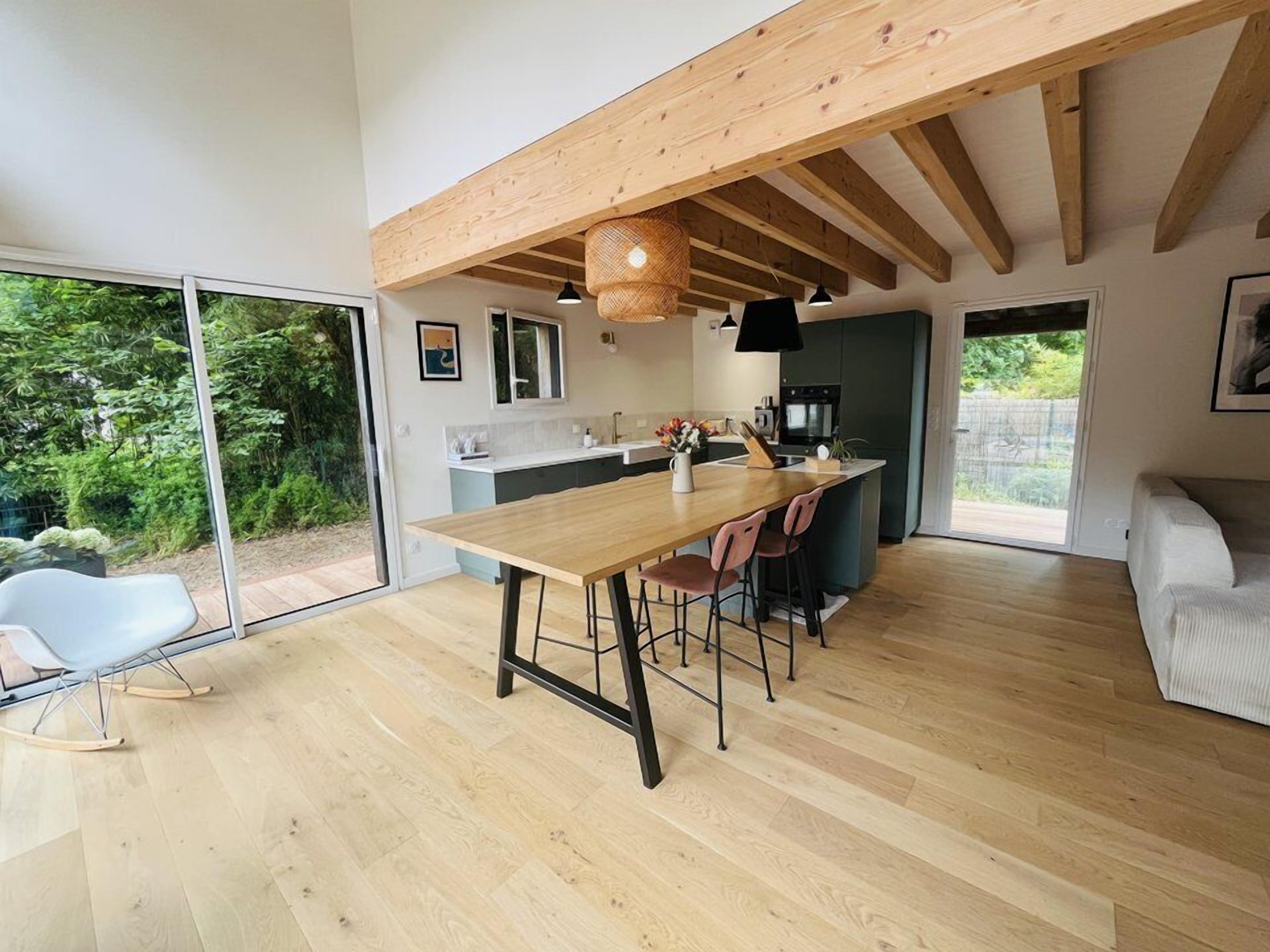 Une cuisine moderne avec un îlot central en bois, de grandes fenêtres et une vue sur la verdure environnante.