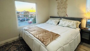 Ein Schlafzimmer mit einem großen Bett, einem Fenster mit Blick auf die Straße, einer Wanddekoration und einer Nachttischlampe.