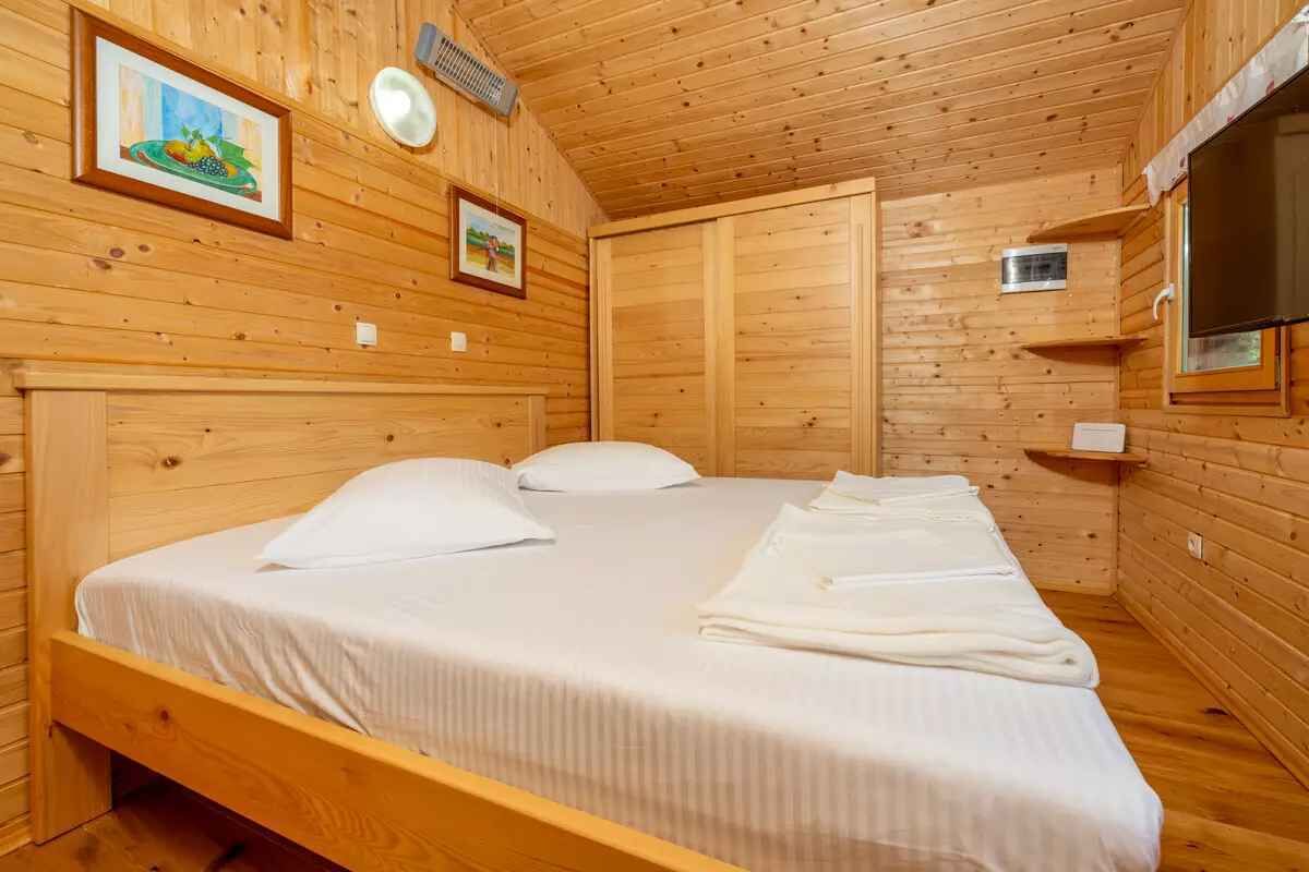 Quarto de cabana de madeira com uma cama de solteiro, um pequeno nicho com espelho e duas molduras na parede.