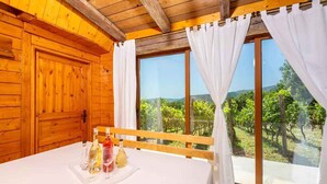 A wooden cabin room with a large window, a table with wine bottles, and a view of a vineyard. - Holiday home with hot tub and sun terrace (Grižane)