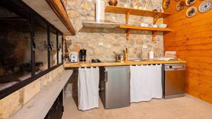 A compact kitchen with a stone wall, wooden shelves, and a small refrigerator. - Holiday home with hot tub and sun terrace (Grižane)