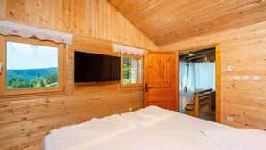 A wooden cabin room with a bed, a TV, and a window with a view of greenery. - Holiday home with hot tub and sun terrace (Grižane)