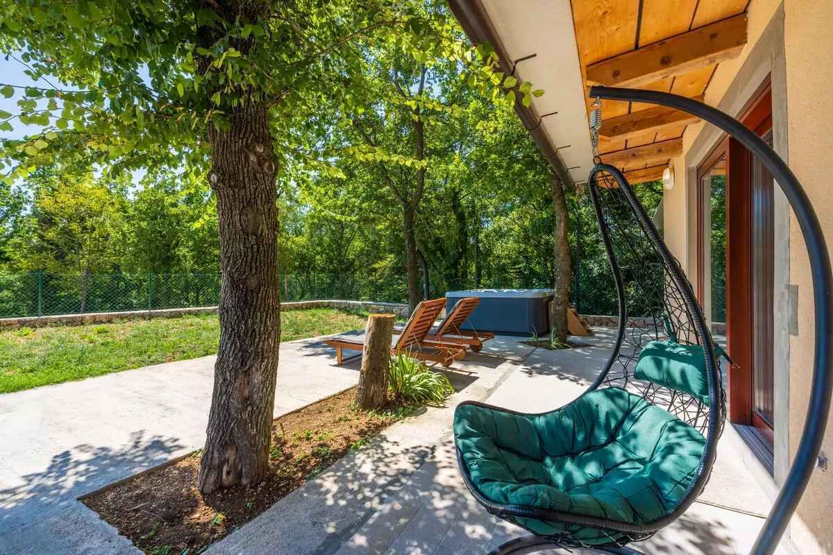 Un espacio al aire libre techado con una silla colgante, un banco de madera y un jacuzzi.