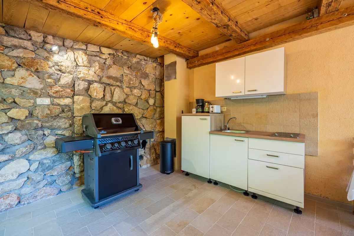A kitchen with a stone wall, a built-in grill, and a white cabinet.