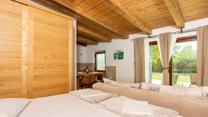 Quarto de hotel com teto de madeira, cama com roupa de cama bem dobrada, sofá com almofada e vista para o exterior através de uma janela.